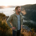 A man pausing on a ridge trail at sunrise, looking out across a misty valley